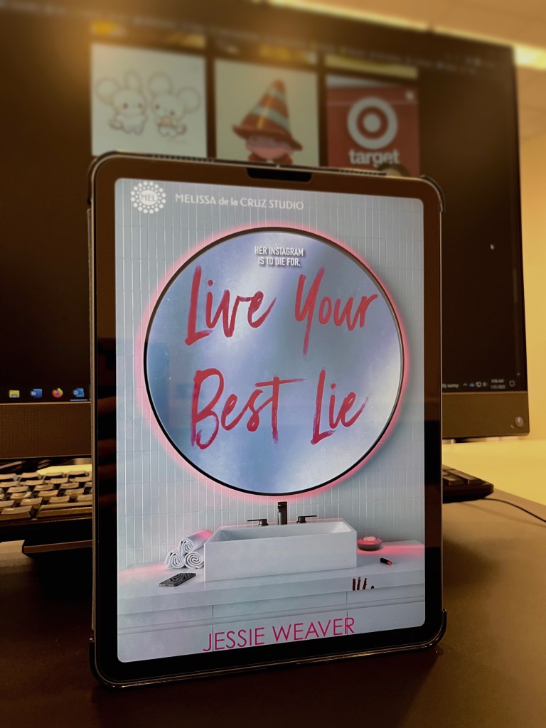Photo of the book cover "Life Your Best Lie: by Jessie Weaver. The cover itself is of a round bathroom mirror with the words "Live Your Best Lie" written in lipstick on the glass. The photo is on an iPad and is in front of a computer screen with Instagram on the screen.