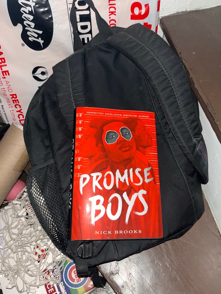 Nick Brooks' YA novel, Promise Boys sits on top a black bookbag